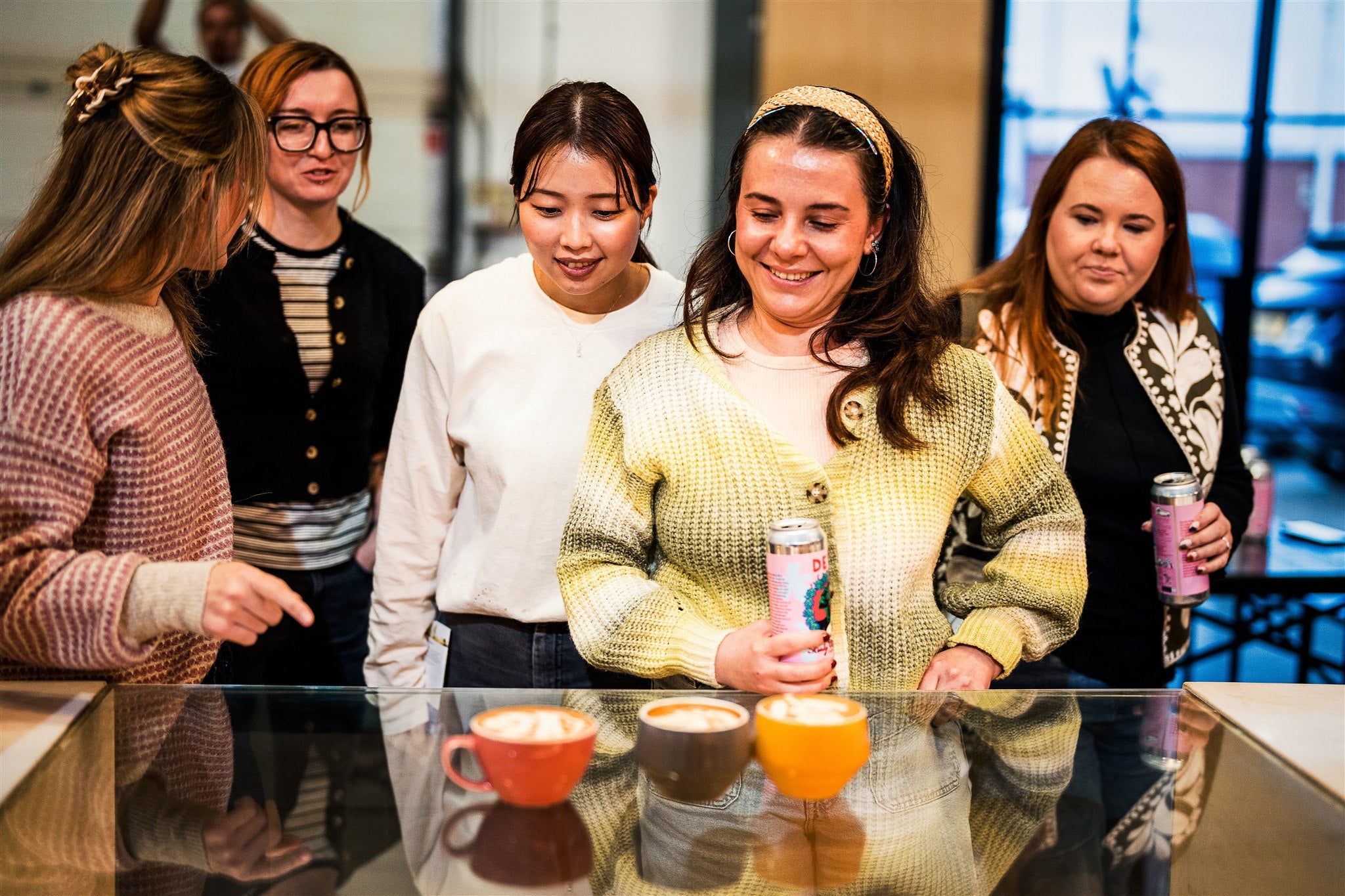 Group of women gathered around a table with coffees smiling and interacting.