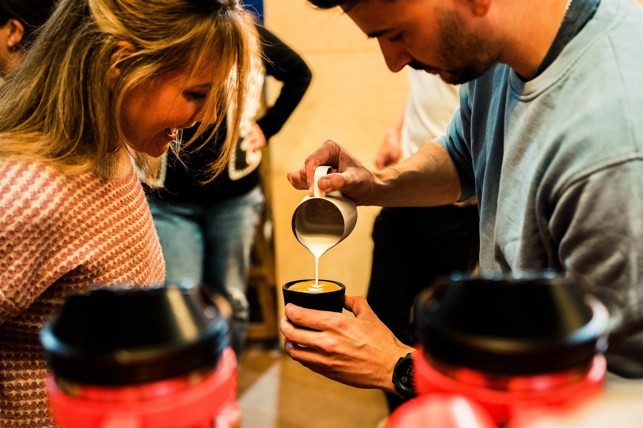 someone doing latte art into a coffee cup while someone watches them